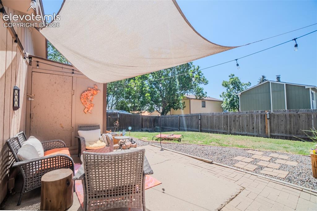 Image 29 of 31: Patio area featuring a neutral-toned sunshade, string lighting, and a paved
