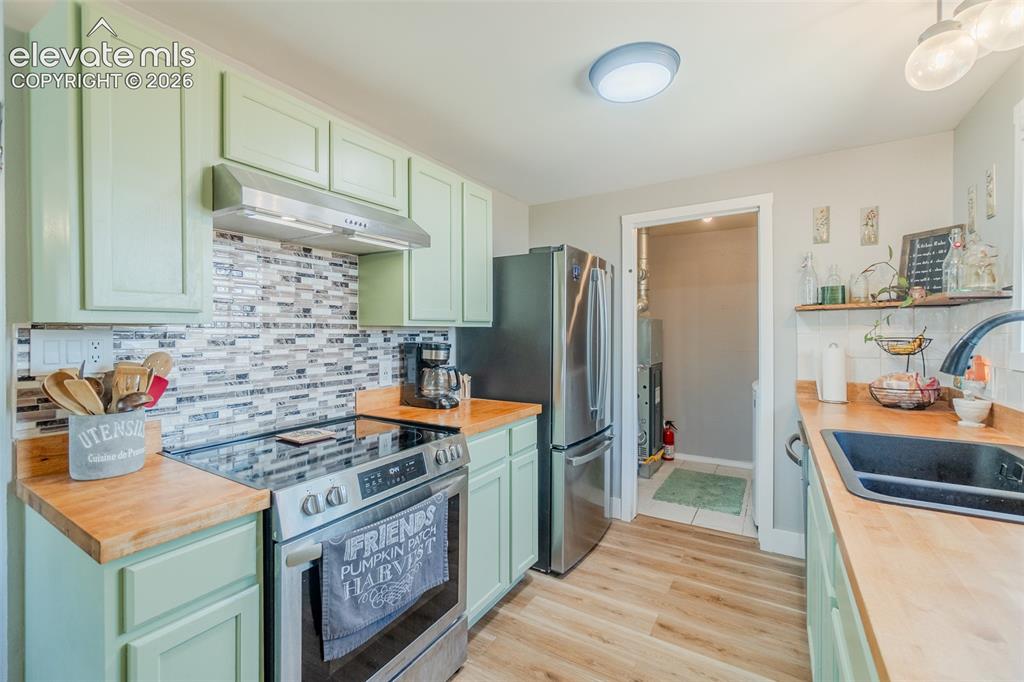 Image 6 of 31: Kitchen featuring light green cabinetry, wood-finish countertops, and a mos