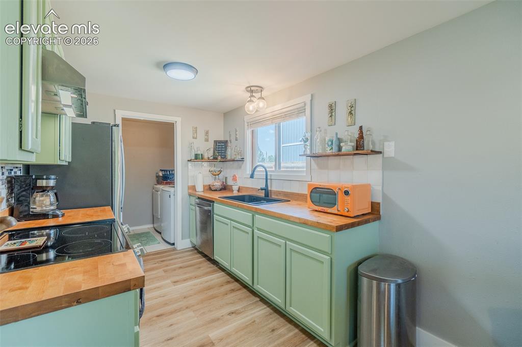 Image 7 of 31: Kitchen featuring light green cabinetry, wood-finish countertops, and stain