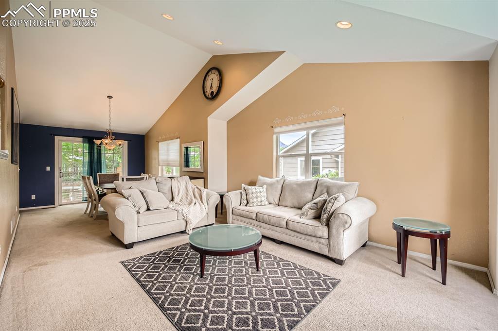 Image 2 of 18: Living area with light carpet, vaulted ceiling, recessed lighting, and a ch