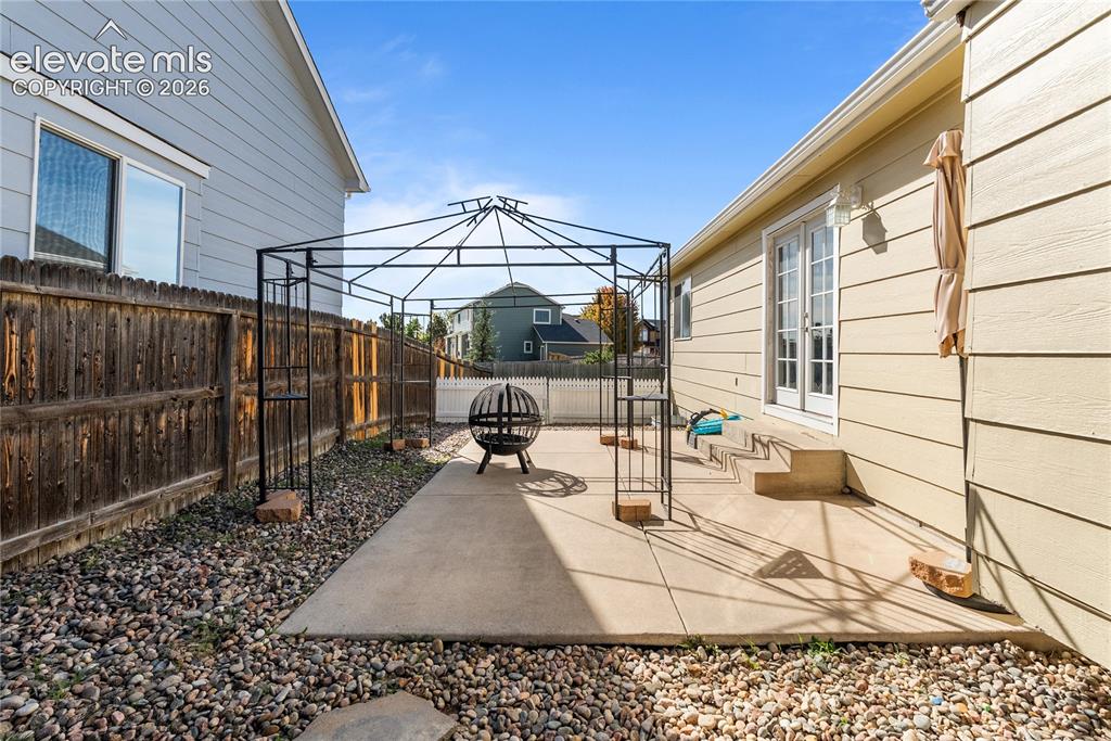 Image 31 of 42: Concrete patio with metal gazebo frame, gravel landscaping, and wood privac