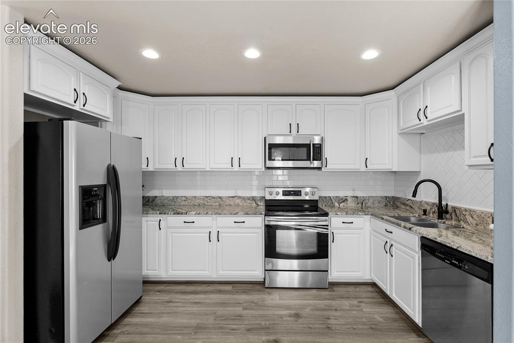 Image 9 of 42: Bright kitchen featuring white cabinetry, stone countertops, stainless stee
