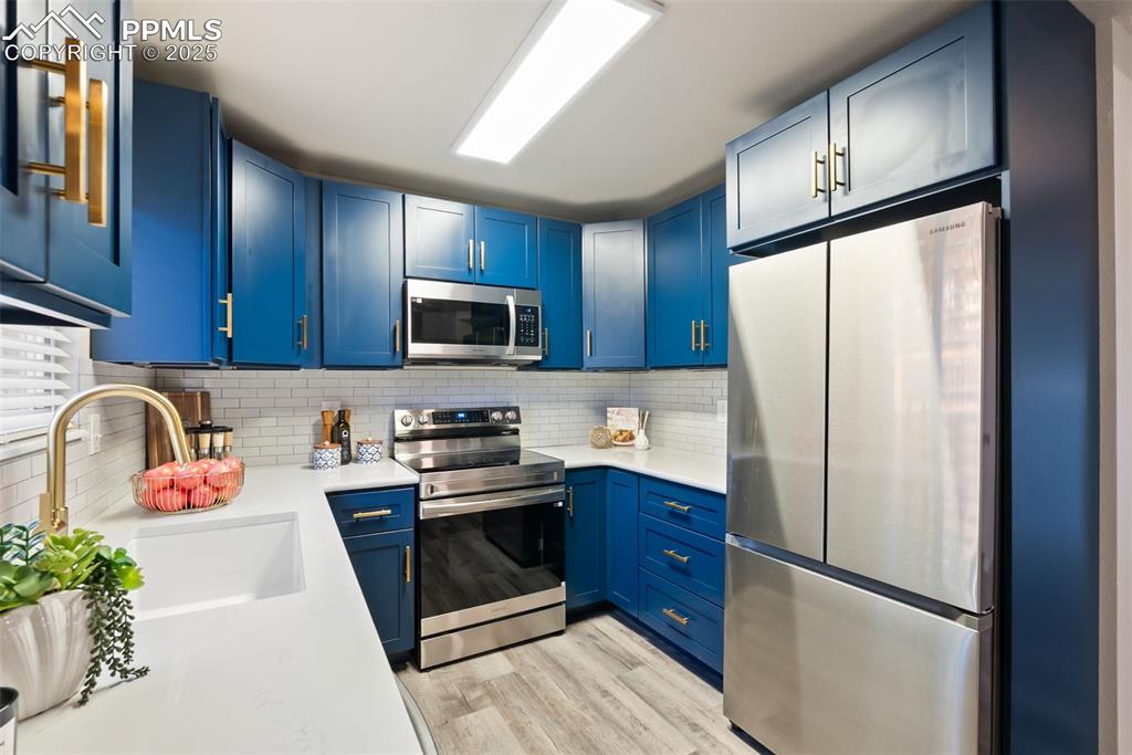 Image 2 of 50: Kitchen with appliances with stainless steel finishes, blue cabinets, taste