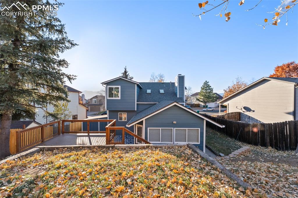 Image 40 of 50: Back of house featuring a chimney, a wooden deck, and a shingled roof