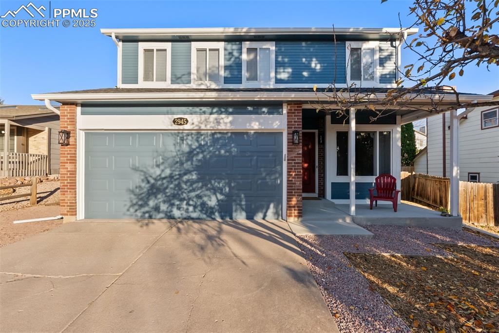 Image 8 of 50: Traditional home with covered porch, driveway, brick siding, and a garage