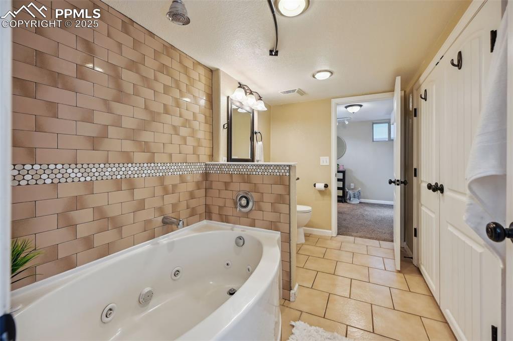 Image 25 of 31: Basement bathroom features granite countertops, jetted tub and overhead sho