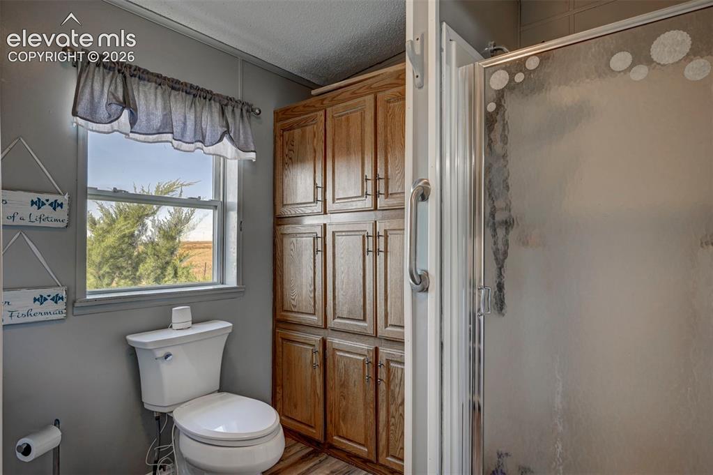 Image 24 of 31: Full bath featuring a textured ceiling, a shower stall, and wood finished f