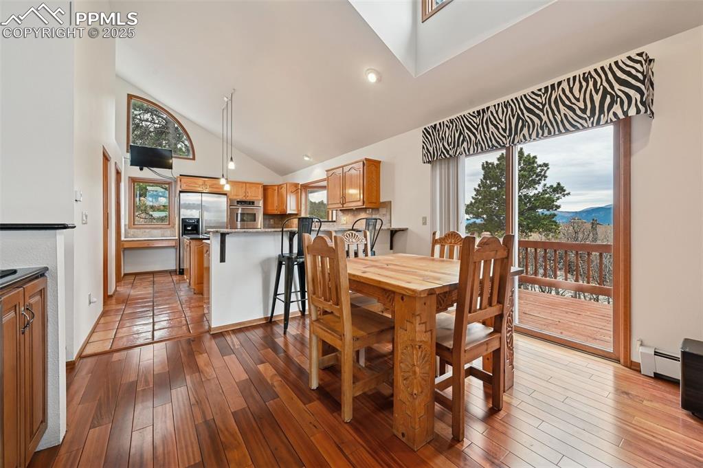 Image 23 of 49: Dining space featuring high vaulted ceiling, light wood-type flooring, base