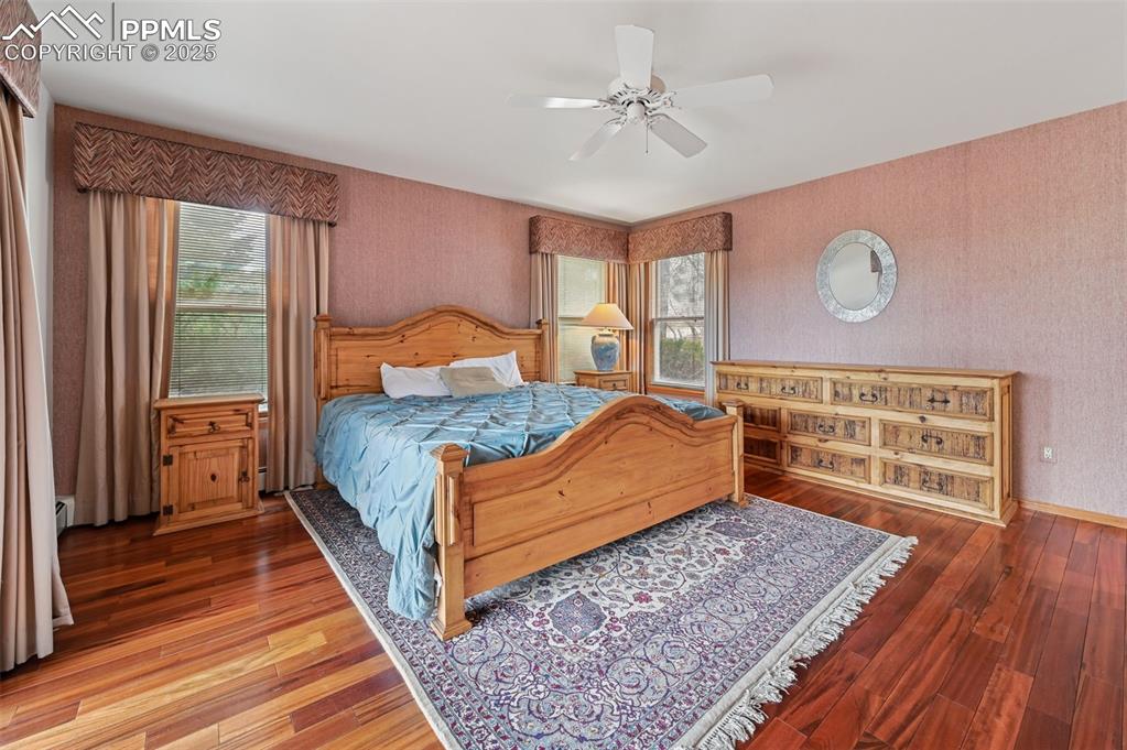 Image 28 of 49: Bedroom featuring wallpapered walls, wood finished floors, a ceiling fan, a