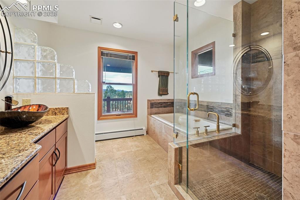 Image 33 of 49: Bathroom with a soaking tub, vanity, a stall shower, baseboard heating, and