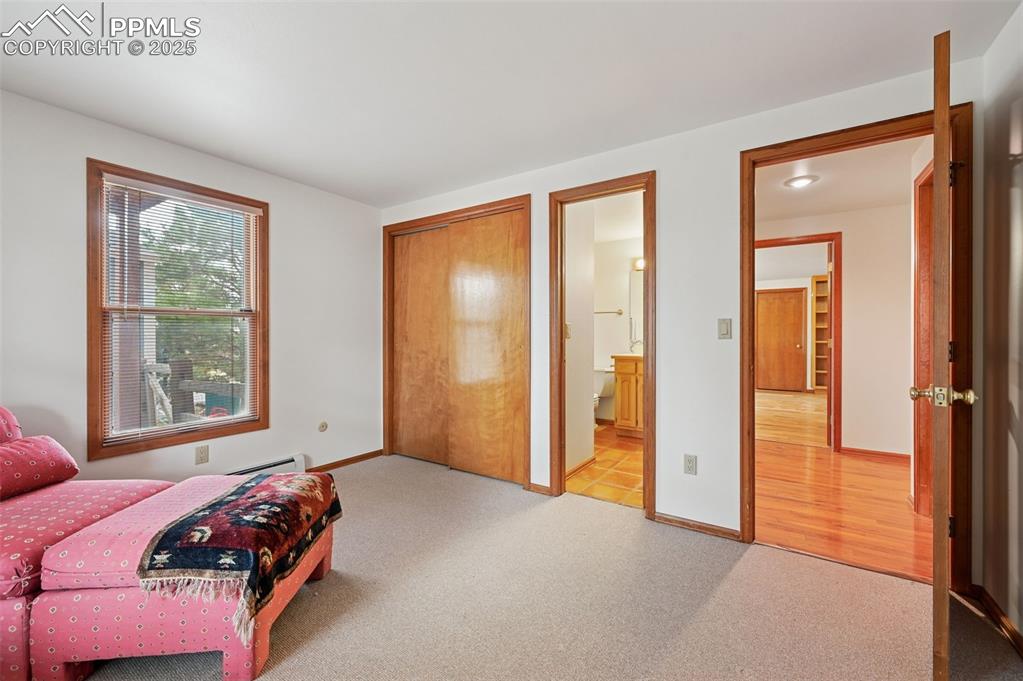 Image 44 of 49: Carpeted bedroom with a closet, connected bathroom, and a baseboard radiato