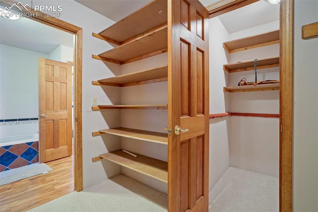 Image 39 of 50: Walk-in closet with extensive built-in shelving, wood-finish doors, carpet
