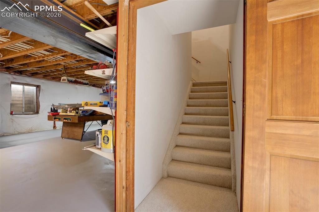 Image 44 of 50: Carpeted staircase with wooden handrail, leading to an upper level