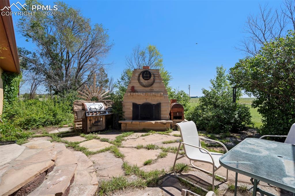 Image 46 of 50: Stone patio featuring a built-in outdoor fireplace and an integrated grilli