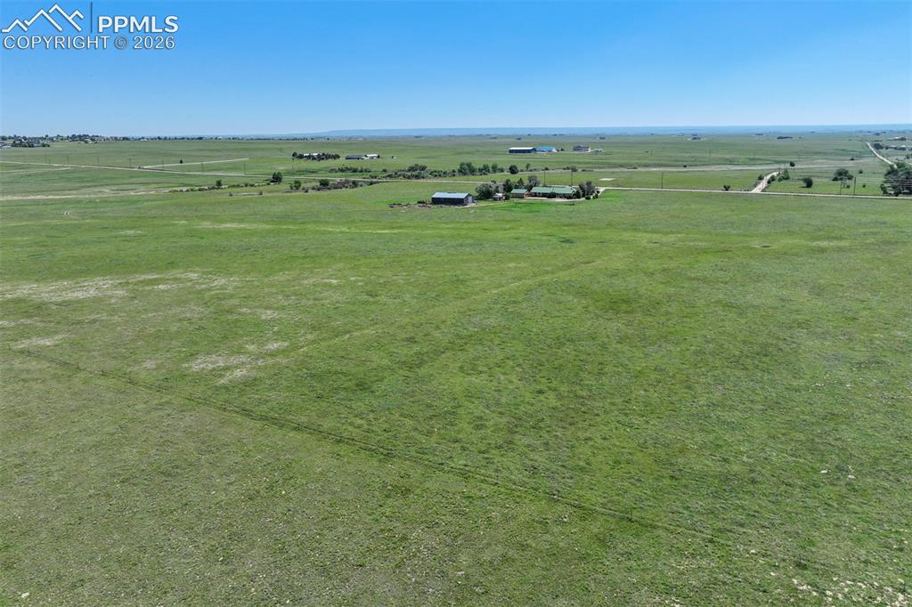 Image 6 of 50: Expansive green acreage featuring a distant residential structure, outbuild