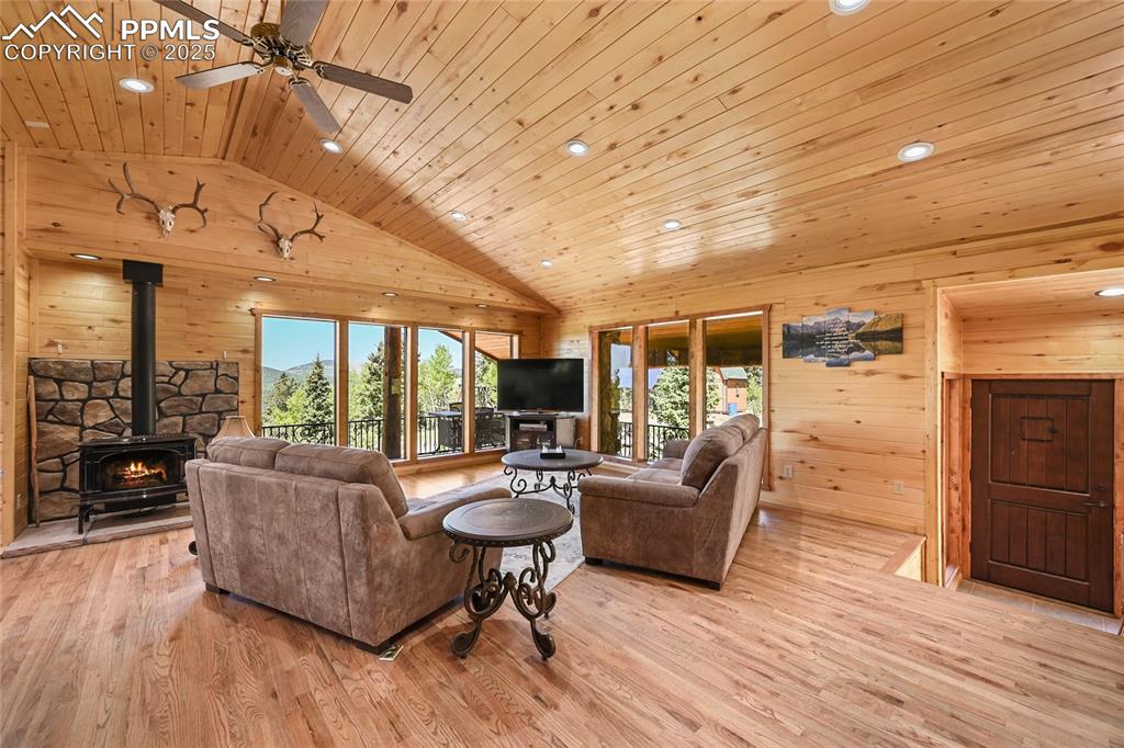 Image 10 of 50: Living area featuring wooden ceiling, a ceiling fan, a wood stove, wood wal