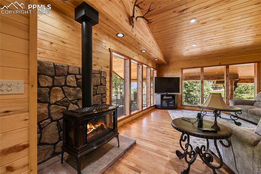 Image 12 of 50: Living room with lofted ceiling, gas stove, wooden ceiling, wooden walls, a