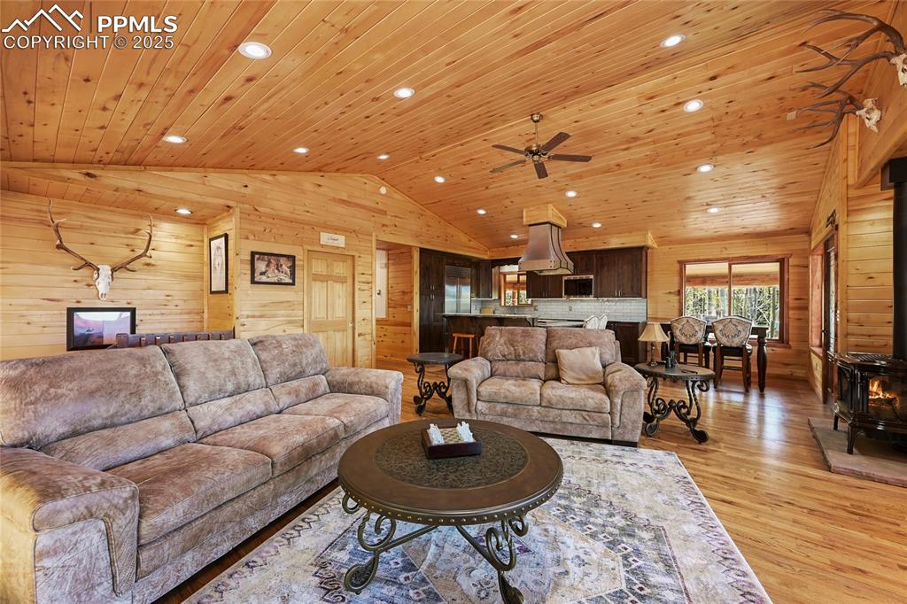 Image 14 of 50: Living room with lofted ceiling, wooden ceiling, wood walls, and light wood