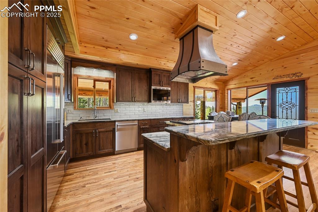 Image 16 of 50: Kitchen with dark stone counters, custom range hood, built in appliances, a