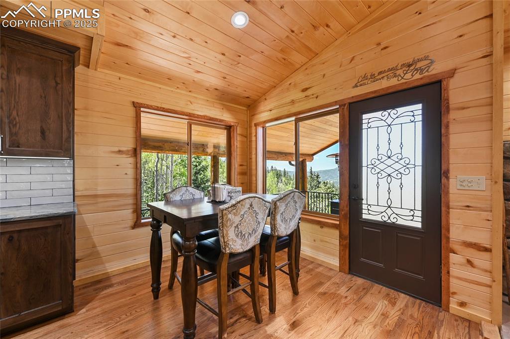 Image 19 of 50: Dining room with light wood-style flooring, wood ceiling, wood walls, and v
