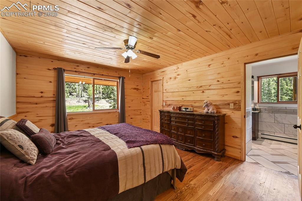 Image 21 of 50: Bedroom with baseboard heating, wood walls, light wood-style floors, and wo