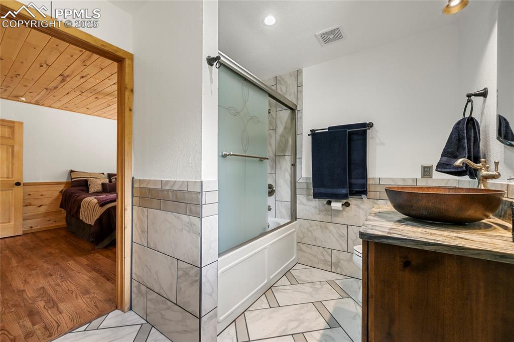 Image 25 of 50: Bathroom featuring tile walls, bath / shower combo with glass door, marble
