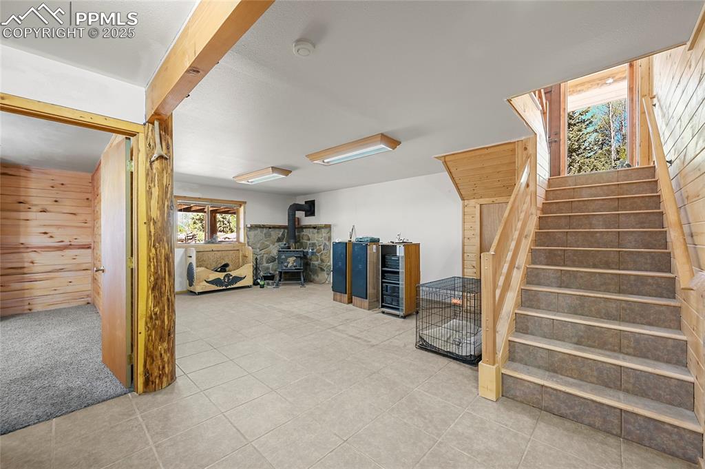 Image 31 of 50: Below grade area with wooden walls, a wood stove, stairway, and tile patter