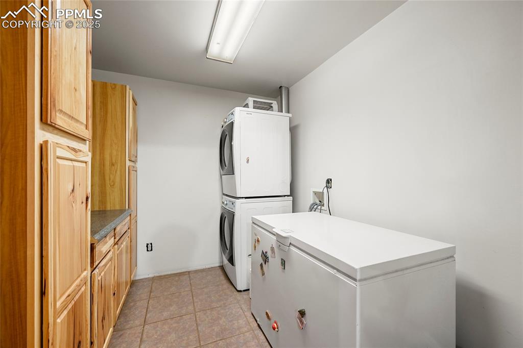 Image 35 of 50: Laundry room with stacked washer / dryer, light tile patterned flooring, an