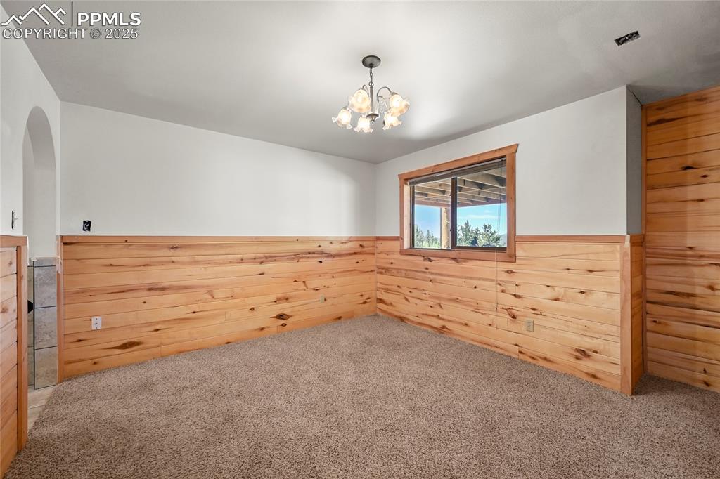 Image 40 of 50: Carpeted spare room featuring a notable chandelier, wooden walls, and wains