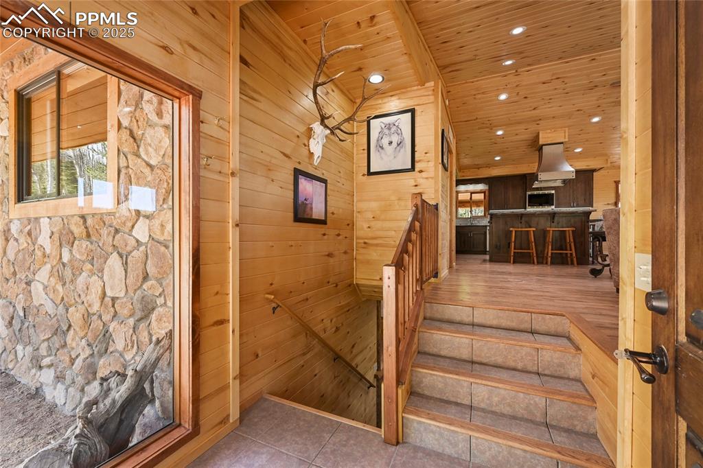Image 8 of 50: Stairway featuring tile patterned floors, wooden ceiling, wood walls, and r