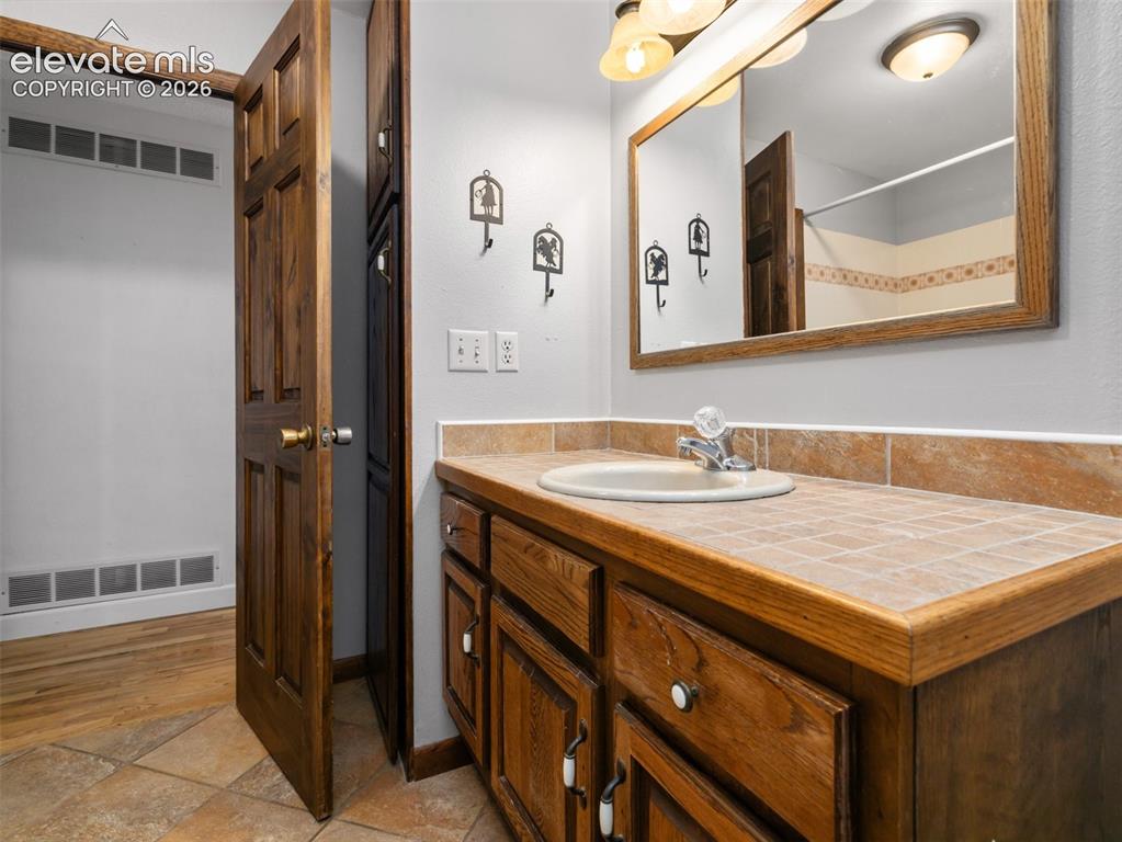 Image 21 of 35: Bathroom vanity featuring a tiled countertop, integrated sink, and wood cab