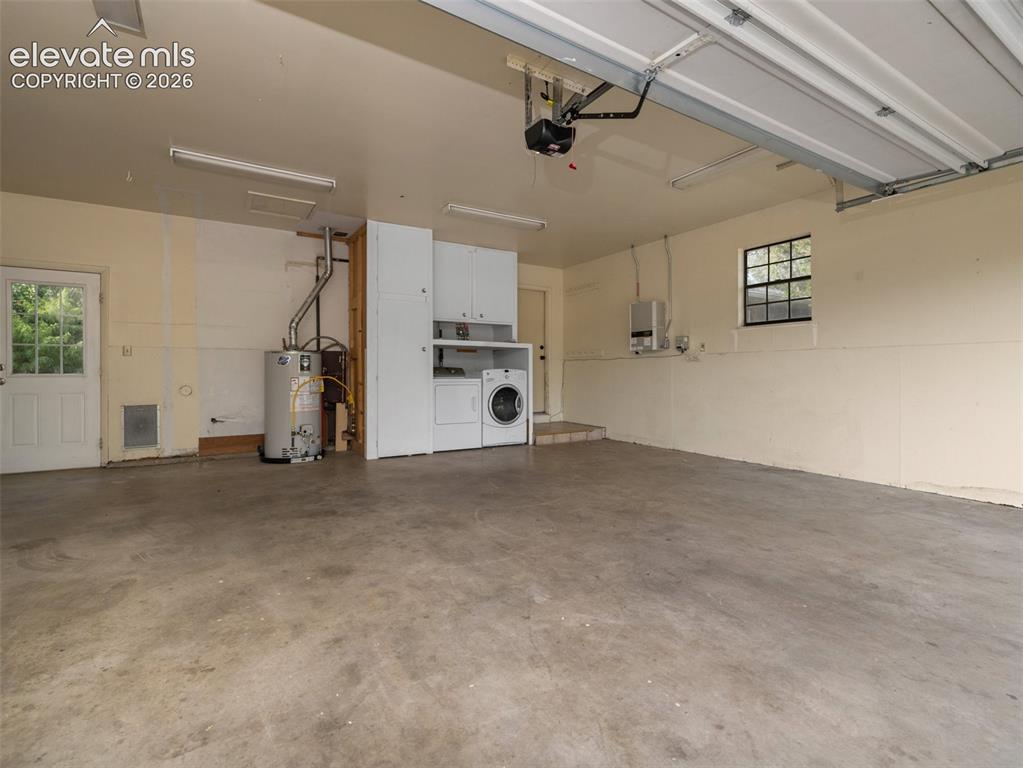 Image 24 of 35: Spacious garage with concrete flooring, overhead fluorescent lighting, and 