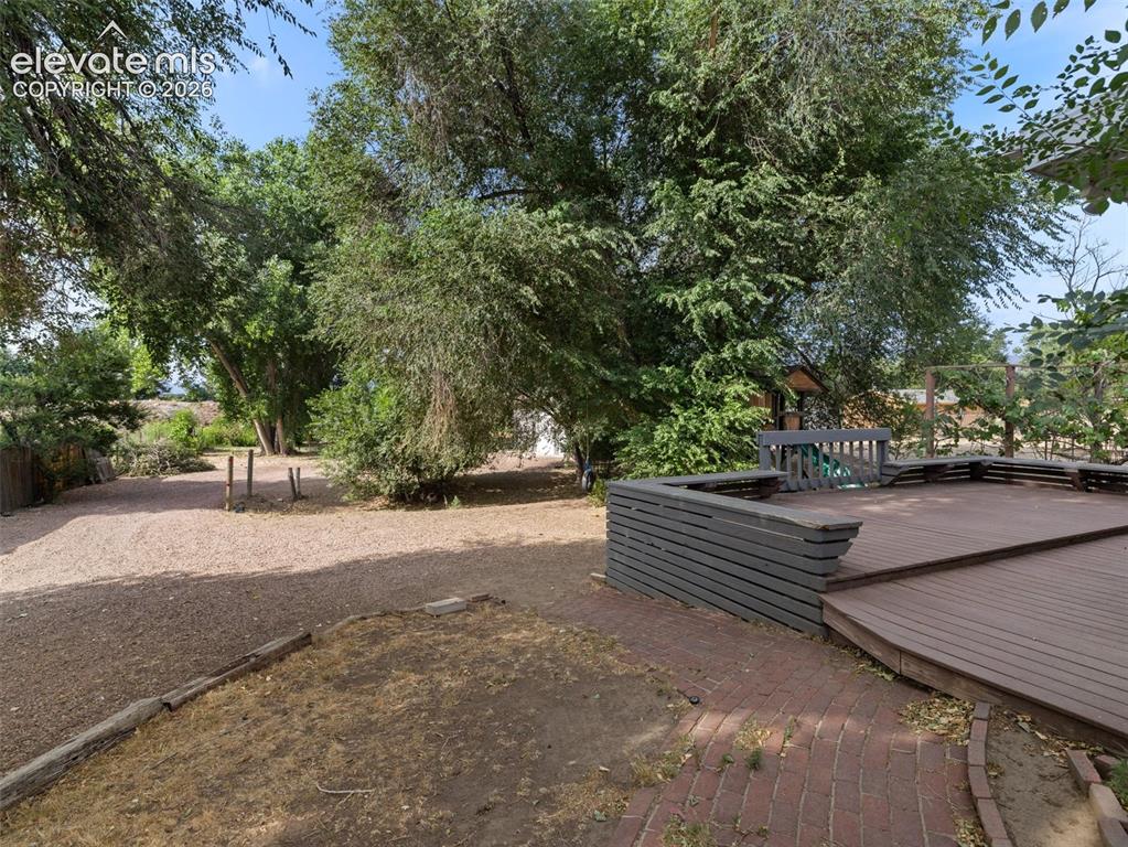 Image 25 of 35: Expansive outdoor deck with built-in seating, surrounded by mature trees, a