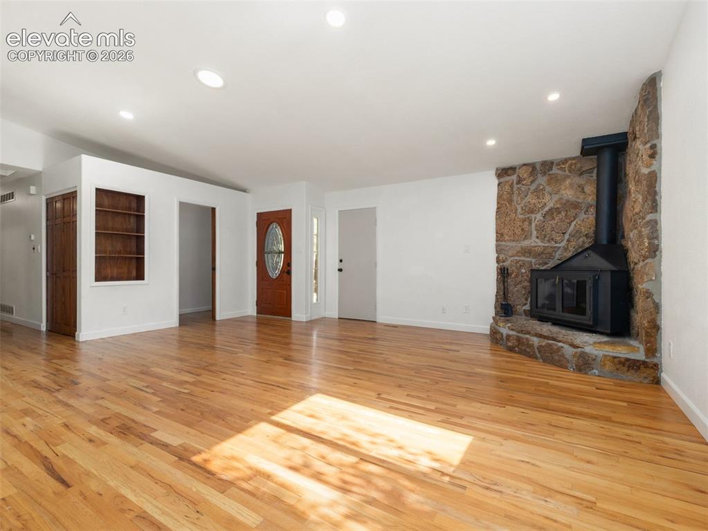 Image 5 of 35: Spacious living area featuring light wood-finish flooring, a stone-clad fir