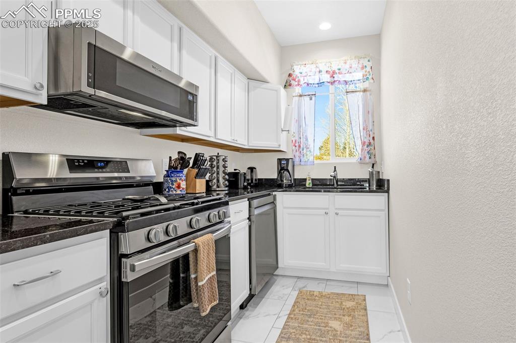 Image 8 of 37: Kitchen featuring dark granite counters, white cabinets, tile floors, and s