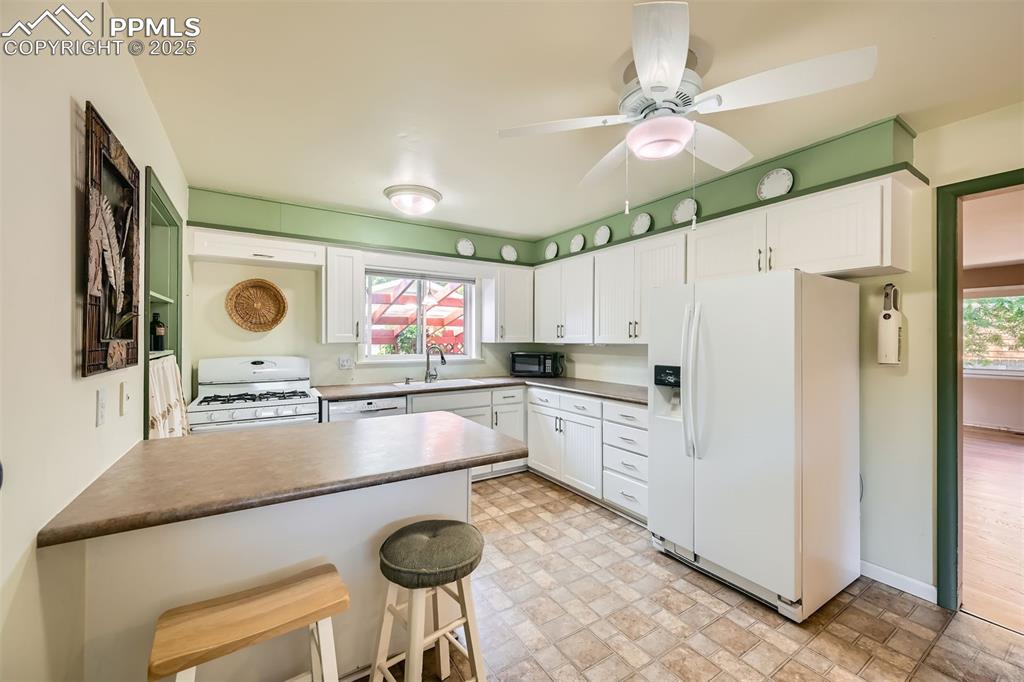 Image 12 of 33: Kitchen with white appliances, a peninsula, white cabinetry, a breakfast ba