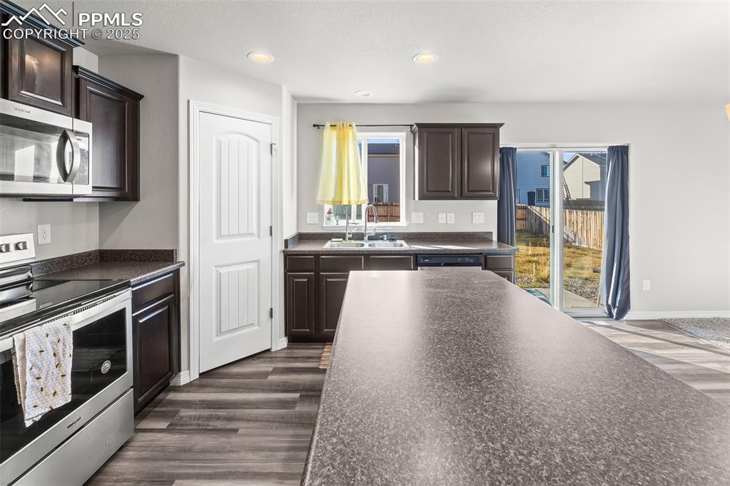 Image 28 of 48: Kitchen featuring stainless steel appliances, dark countertops, dark brown