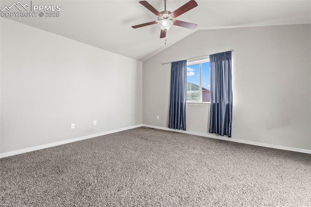 Image 32 of 48: Carpeted empty room featuring vaulted ceiling and a ceiling fan