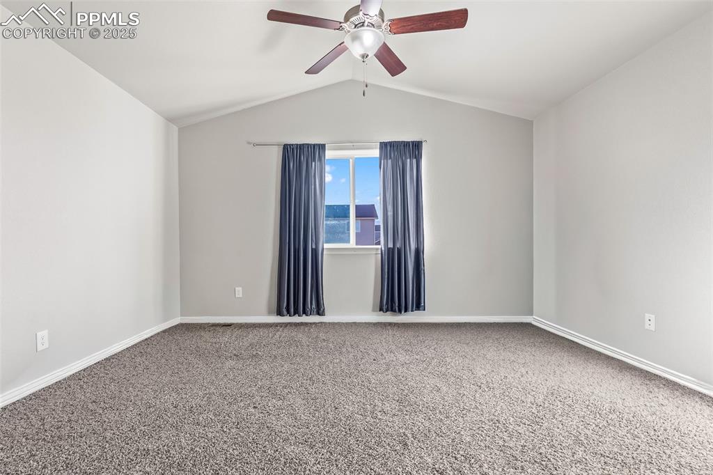 Image 33 of 48: Carpeted spare room featuring vaulted ceiling and ceiling fan