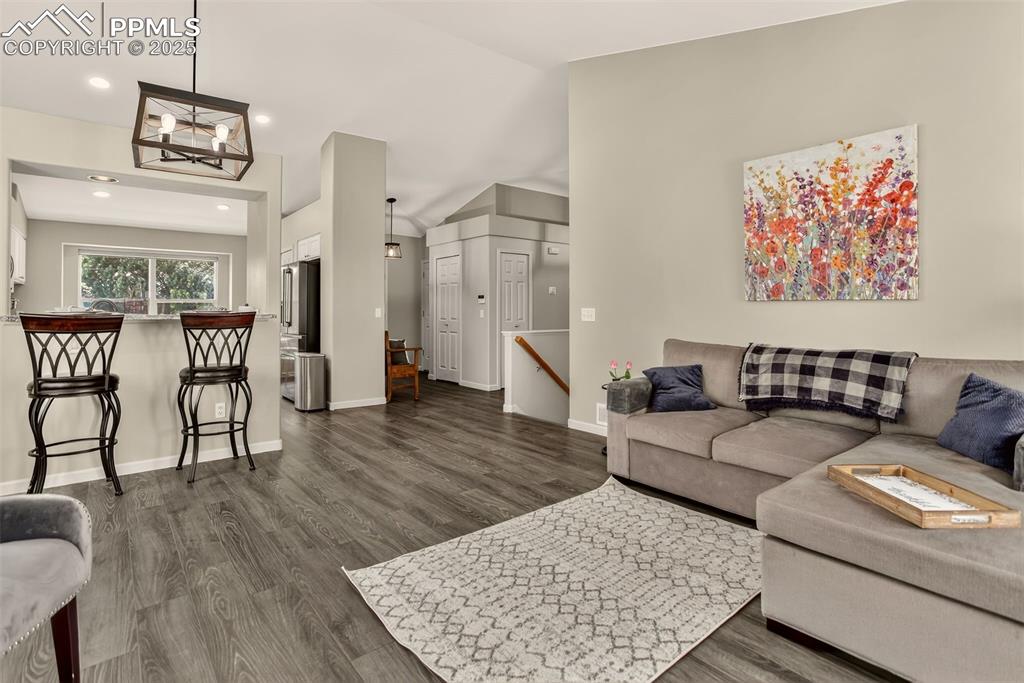 Image 11 of 38: Living area with dark wood-type LVP flooring, vaulted ceiling, and recessed