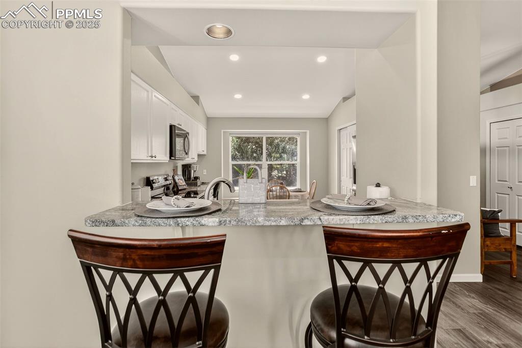 Image 12 of 38: Kitchen featuring a kitchen breakfast bar, white cabinets, dark wood LVP fl