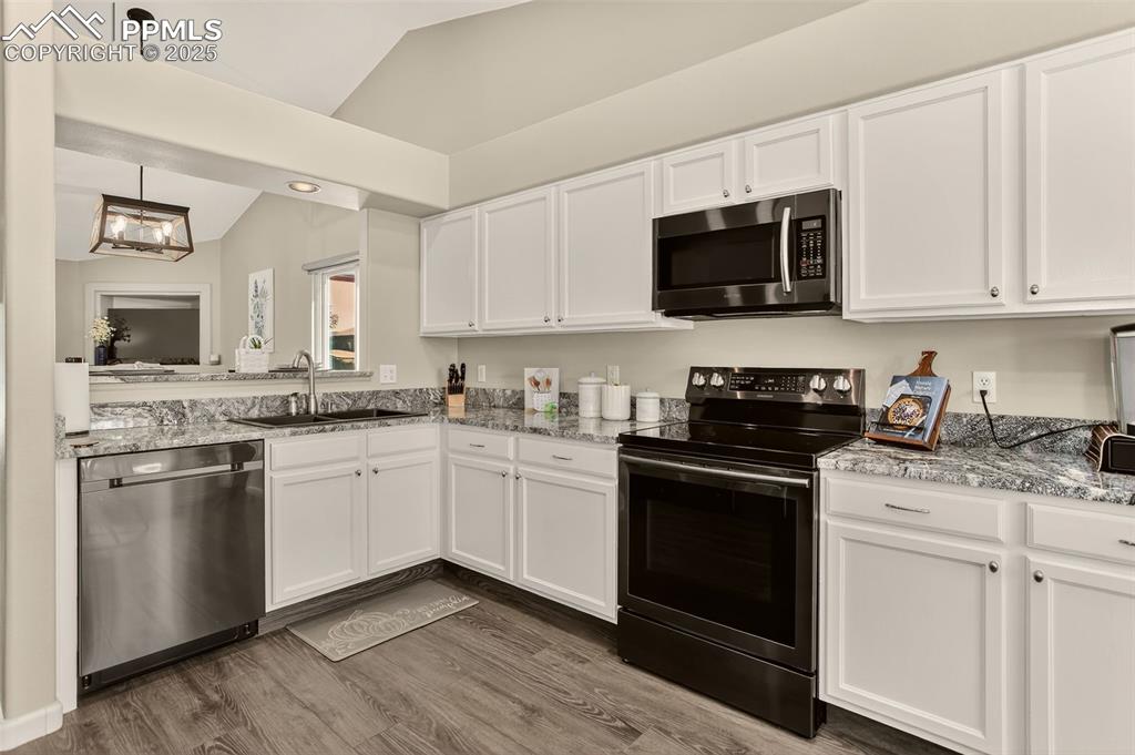 Image 16 of 38: Kitchen featuring stainless steel appliances, white cabinetry, lofted ceili