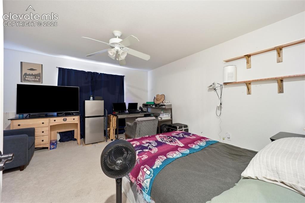 Image 21 of 49: Carpeted room with a ceiling fan, window with dark drapes, and built-in she