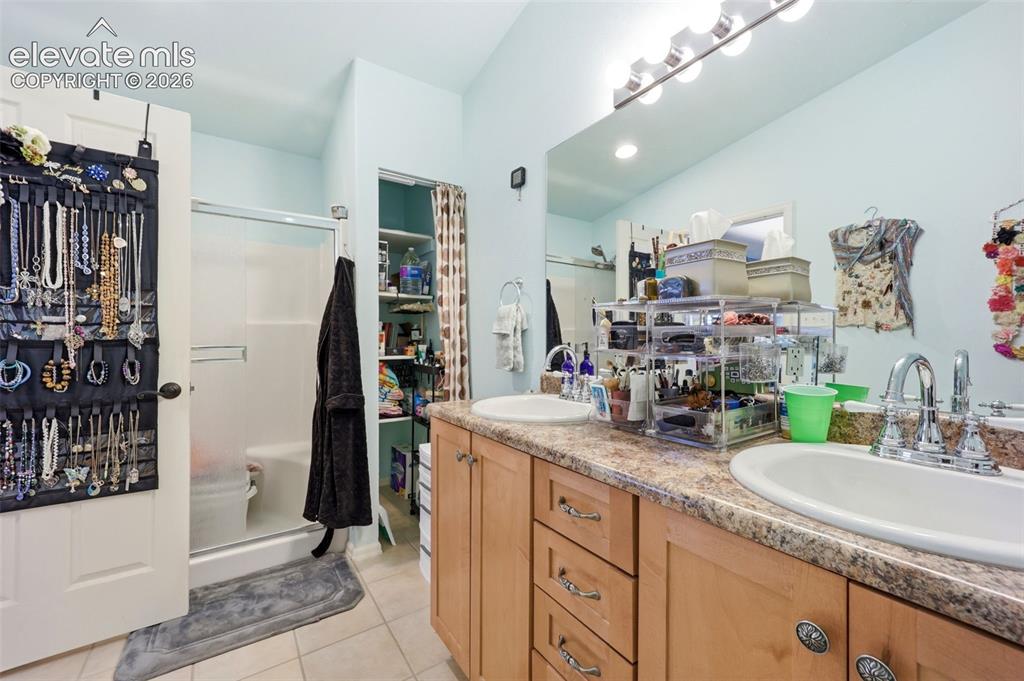 Image 23 of 49: Bathroom featuring a dual vanity with light wood cabinetry, a shower with a