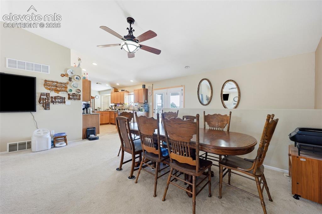 Image 5 of 49: Dining area with a wood-finish ceiling fan, neutral carpet flooring, and a