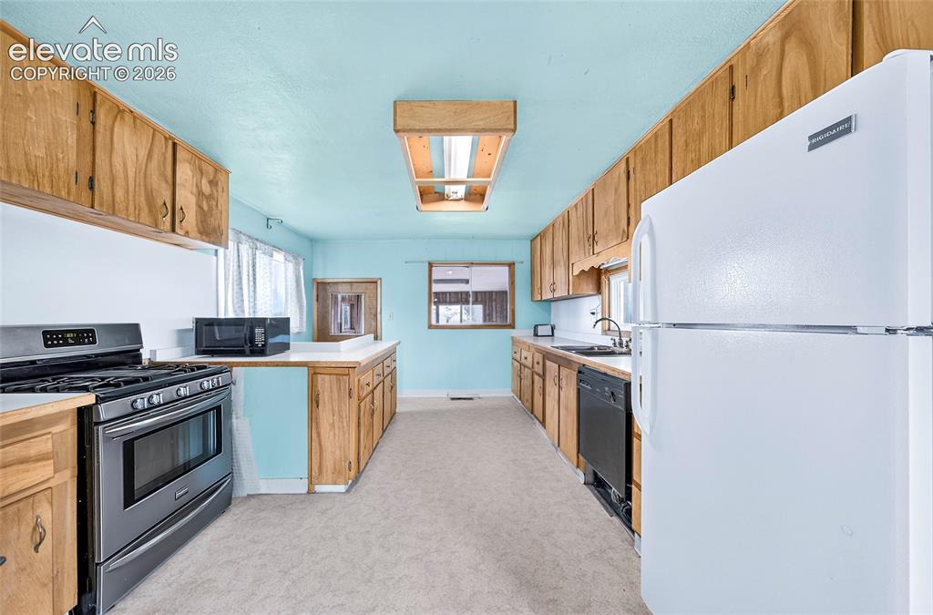 Image 13 of 45: Galley kitchen with wood cabinetry, stainless steel range, white refrigerat