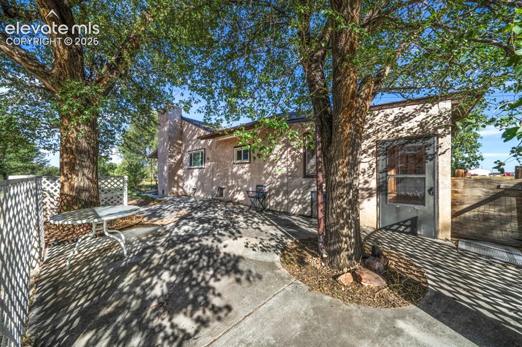 Image 31 of 45: Stucco exterior with concrete patio, white lattice fencing, and mature tree