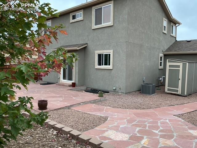 Image 4 of 29: Rear view of house with stucco siding, a storage unit, and a patio area