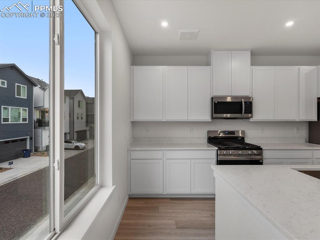 Image 9 of 32: Kitchen featuring stainless steel appliances, white cabinets, light wood-st