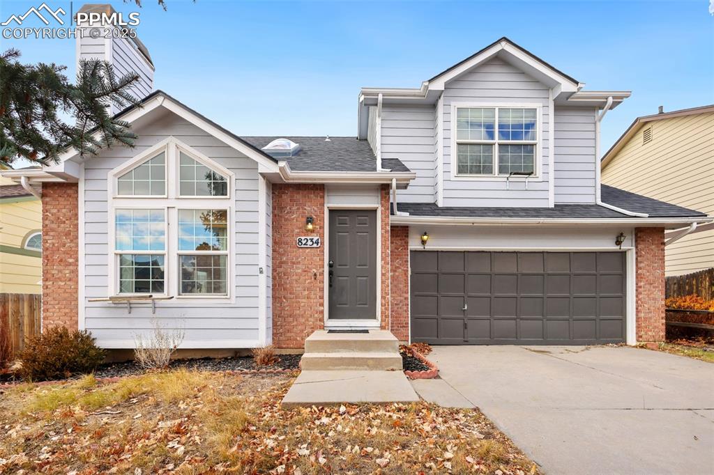 Caption: View of front facade with brick siding, roof with shingles, an attached garage, and driveway